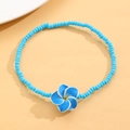 Detalle de la tobillera de cuentas azules con colgante de flor de plumeria sobre amarillo - Azul