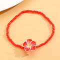 Detalle de tobillera de cuentas rojas con colgante de flor de frangipani en fondo naranja cálido - Rojo