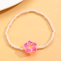 Detalle de tobillera bohemia de cuentas con colgante de flor de plumeria rosa sobre fondo cálido - Rosa Roja