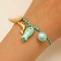 Detail of hand-woven bracelet with ceramic fish and gold dolphin charms on wrist - Green Ocean Pendant (19 Green 1611)
