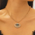 Detailed close-up of golden evil eye pendant with blue crystals on model neckline - Necklace / Gold