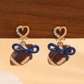 Detail of rugby heart earrings with blue bows and rhinestones on wood display - Blue Bow Football Earrings (0081)