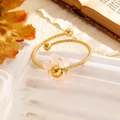 Details des goldfarbenen Hammerschlag-Armreifs mit zarter rosa Kristallblume auf Display - Weiß