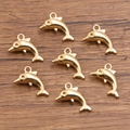 Set mit sieben goldenen Delfinanhängern für DIY-Schmuck auf dunkler Holzoberfläche - Delfinform (Nr. 16) / 11*17mm / Gold