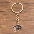 Gold-tone keychain with black graduation cap charm and red tassel on wood background - Style 9 (20X22mm)