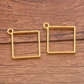 Paar vierkante goudkleurige hangers voor DIY-sieraden op een houten achtergrond - Kleine kubus