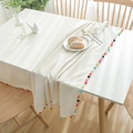 Primer plano del mantel de lino beige con pompones de colores sobre mesa de madera - 60x60 / Beige (Pompones Coloridos)