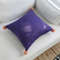 Square dark purple cotton linen pillow with orange-pink pom-poms on a white sofa - 45x45cm / Purple with Orange Pom-poms