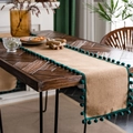 Natural jute table runner with dark green pom pom trim on a vintage wooden table - Natural Jute With Green Pom-poms
