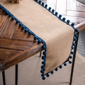 Natural burlap table runner with navy blue pom-pom fringe on a rustic wooden table - Natural Jute With Navy Pom-poms
