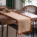 Natural jute table runner with vibrant orange pompom trim on wooden dining table surface - Natural Jute With Orange Pom-poms / Round Placemat 30
