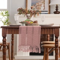 Pink bohemian woven table runner with tassel details on a dark wooden dining table - 33x120