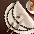 Semi-circular beige linen placemat with black pom-pom trim and rustic embroidery details - Black Thread
