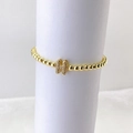 Detalle macro de una pulsera de cuentas doradas con un colgante de letra H con micro pavé - Oro H
