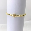 Primer plano detallado de una pulsera elástica de cuentas doradas con un dije de letra T en pavé - Oro T