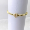 Detalle de pulsera elástica con cuentas doradas y un dije de letra U con circonitas incrustadas - Oro U