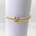 Primer plano de pulsera dorada de cuentas con dije de mariposa micro-pave en base blanca - Oro X