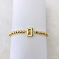 Detail view of 18k gold beaded elastic bracelet featuring a polished number eight charm - Letter B