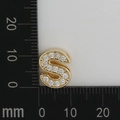 Detail shot of a gold-tone 'S' letter charm with micro zircons next to a ruler - S