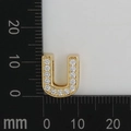 Macro shot of 11x13mm gold plated letter U pendant with white zircon stones on a scale - Letter U
