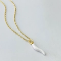 Detailed macro view of a gold-plated necklace featuring a white resin cornicello pendant - White Chili Style