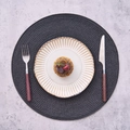 Detalle de mantel individual redondo con plato de cerámica y cubiertos de madera - Pieza única / Negro