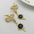 Detailed shot of golden snake drop earrings with blue evil eye charms on white base - Bright Blue (Style B)