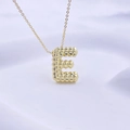 3D-strukturierte goldene Halskette mit Buchstaben-E-Anhänger auf weißem Stoffhintergrund - Gold E