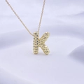 Goldene Halskette mit K-Buchstaben-Anhänger und polierter Perlentextur auf weißem Stoff - Gold K