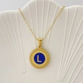 Collana dorata con ciondolo in smalto blu lettera L e bordo intrecciato su vassoio a conchiglia - Lettera L / Blu