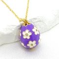 Detail of purple enamel Easter egg pendant with white flower design on gold chain - Purple