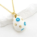 Macro view of a 14K gold-plated Easter egg pendant with blue evil eye enamel and stars - White
