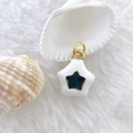 Macro detail of star shaped enamel pendant with gold loop on soft white plush background - Star #3