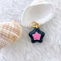 Detailed view of a black and pink enamel star pendant on soft white fabric with sea shells - Star #7