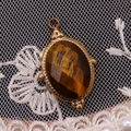 Detail eines ovalen Tigerauge-Anhängers mit goldenem Seilrand und Perlenverzierung - 15x24mm / Tigerauge