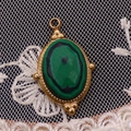 Detail eines vergoldeten ovalen Anhängers mit Malachit-Stein auf Spitzenhintergrund - 15x24mm / Malachit