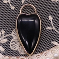 Macro shot of an elongated black heart-shaped stone pendant with gold metal edges - Black Agate