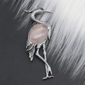 Primer plano de broche de grulla en plata con cuarzo rosa ovalado sobre piel blanca y negra - Cuarzo rosa