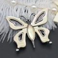 Détail macro d'une broche papillon avec nacre irisée et découpes de cœur en métal argenté - 41x48mm / Nacre Blanche