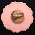 Macro shot of circular picture stone pendant with golden plated edge on a pink lace mat - Jasper