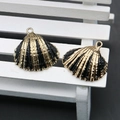 Close-up of scallop shell charms with gold plating and black enamel on white wood - Black
