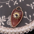 Macro shot of heart-shaped reddish stone pendant with golden evil eye and lace decor - Watermelon Quartz