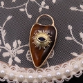 Macro shot of tiger eye stone heart pendant with gold evil eye inlay on lace background - Tiger's Eye