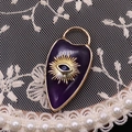 Macro shot of purple enamel heart pendant with golden evil eye on white lace - Purple Crystal