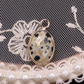 Macro shot of faceted dalmatian jasper oval pendant with gold edge on lace background - 11x19mm / Dalmatian Jasper