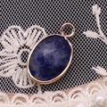 Macro view of oval faceted lapis lazuli pendant with rose gold plated metal on lace - 11x19mm / Blue Sodalite