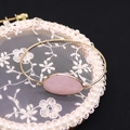 Vista macro detallada de una piedra de cuarzo rosa ovalada en un brazalete dorado abierto - Cuarzo rosa