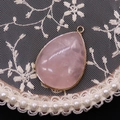Close-up of teardrop rose quartz pendant with gold electroplated edges on lace fabric - Rose Quartz