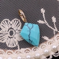 Vue macro d'un pendentif en turquoise avec bordure dorée sur fond de dentelle blanche - Turquoise Bleue