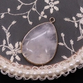 Macro shot of a teardrop rose quartz pendant with gold metal frame on white lace - White Crystal